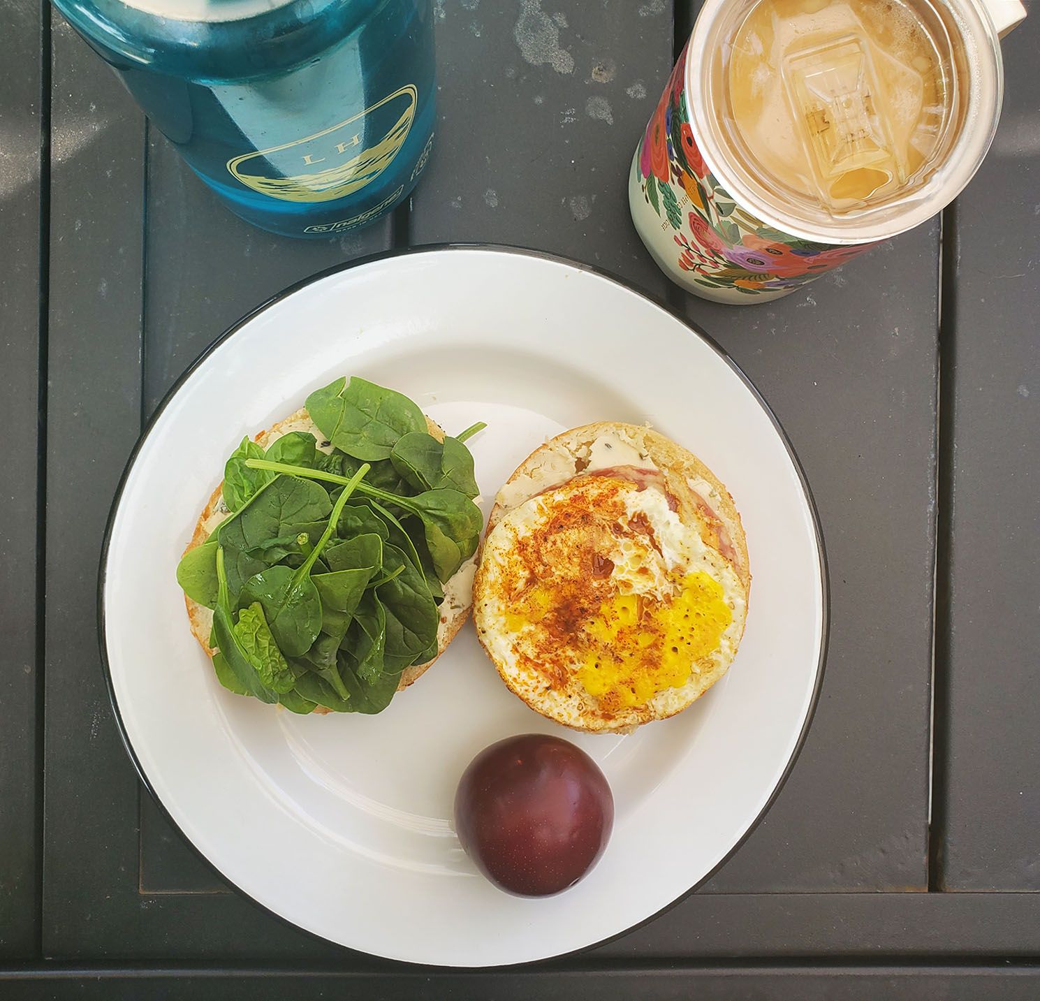 plum and bagel with fried egg and spinach on a plate next to cup of coffee and water bottle