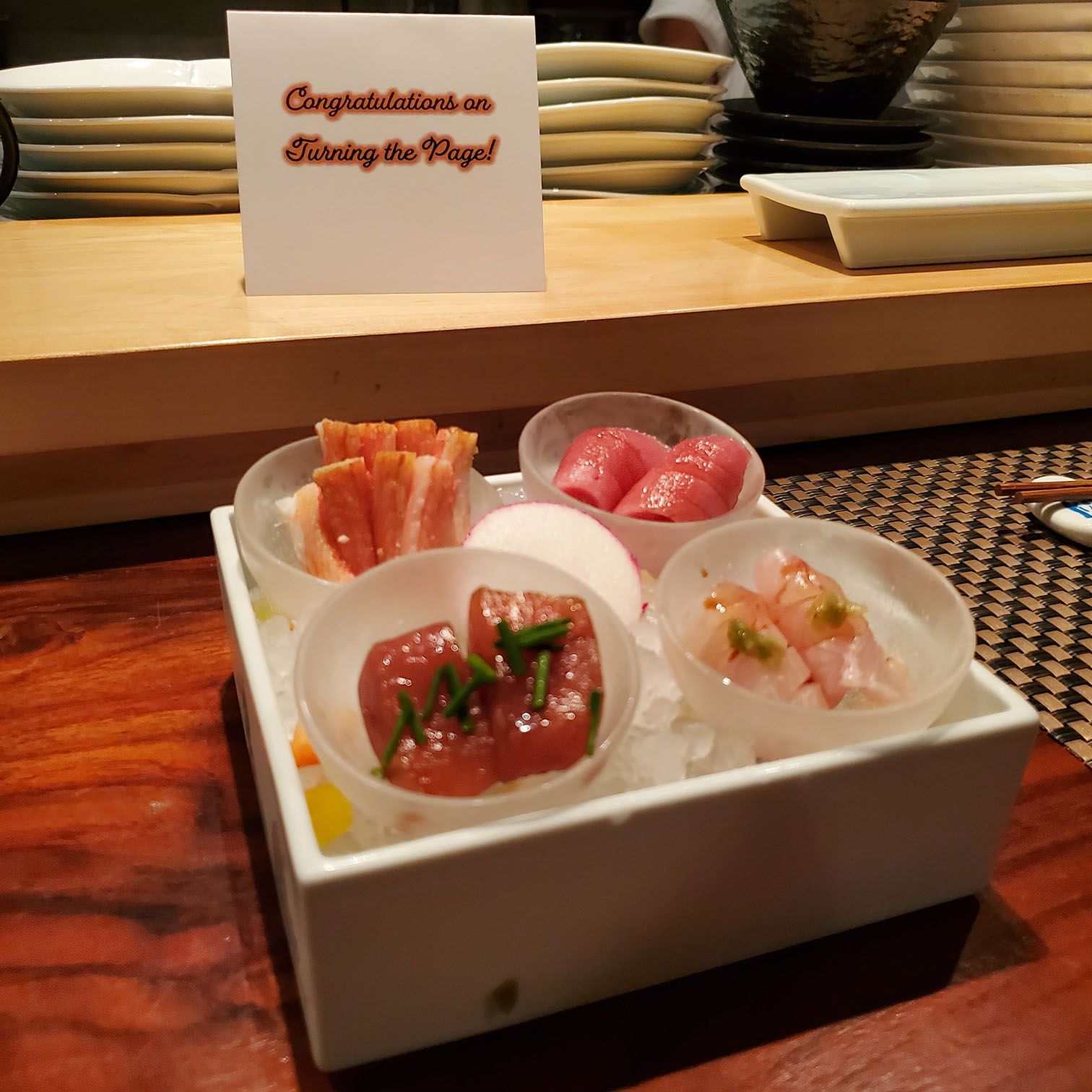 four types of sashimi with a sign that says "congrats on turning the page"