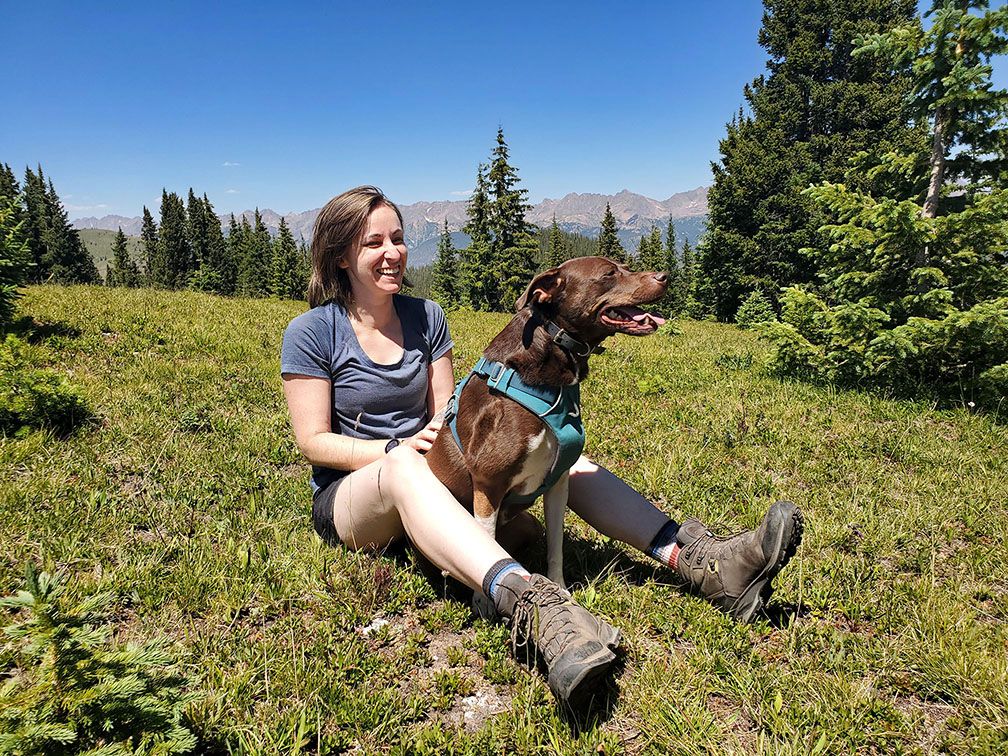 juliane and a brown dog sitting in grass with mountains and trees in background